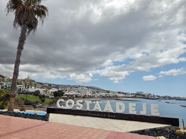 Enseigne de Costa Adeje Enseigne de Costa Adeje Tenerife Sur face à la mer, avec des hôtels et des bâtiments touristiques en arrière-plan.